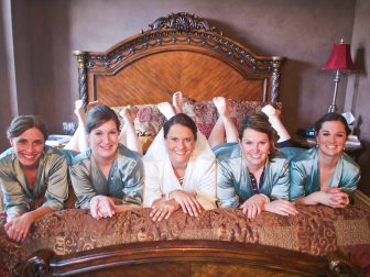 smiling bride and bridesmaids laying on bed